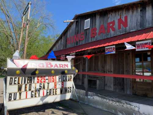 A rustic building with a sign for "Wing Barn," advertising delivery, pickup, and a buy-one-get-one-free wings deal.