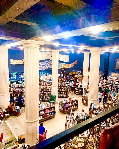 A spacious bookstore with tall columns, shelves of books, and people reading and browsing in a vibrant atmosphere.