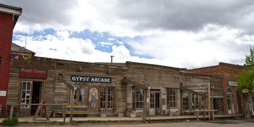 A row of rustic wooden buildings with signs for "Gypsy Arcade" and "Ruby Chang," under a cloudy sky.