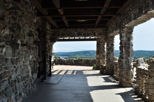Stone archway with wooden beams, overlooking a scenic landscape of hills and blue sky.