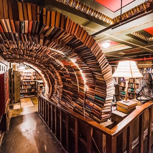 A cozy library with a unique archway made of stacked books, illuminated by warm lighting.