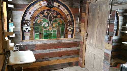 A rustic bathroom featuring a stained glass window, wooden walls, and a vintage sink.