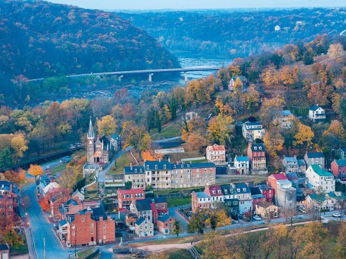 Aerial view of a picturesque town with autumn foliage, a river, and a bridge in the background.