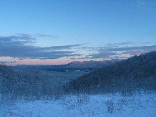 A serene winter landscape with snow-covered hills under a blue sky and soft pink clouds at dusk.