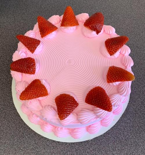 A round pink cake topped with whipped cream and fresh strawberries arranged in a circle.