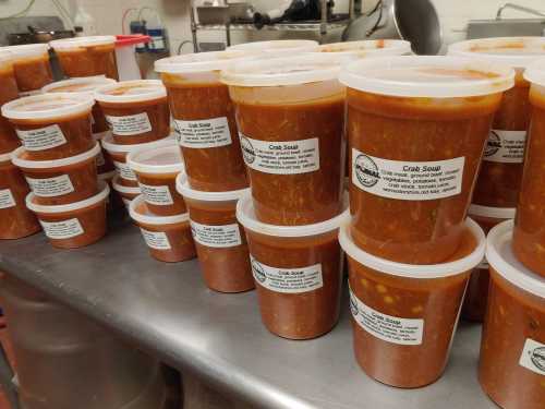 Containers of crab soup lined up on a kitchen counter, each labeled with ingredients and storage instructions.