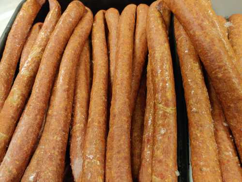 A close-up of several long, reddish-brown sausages arranged closely together on a black tray.