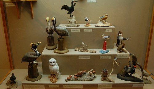 A display of intricately carved bird figurines on a shelf, showcasing various species and artistic styles.