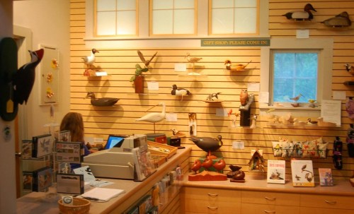 A gift shop interior featuring wooden bird carvings on the walls and a counter with a cashier.
