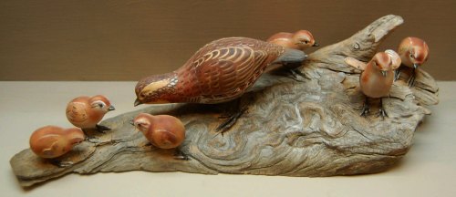 A wooden sculpture of a bird and four chicks on a textured base, showcasing intricate details and craftsmanship.