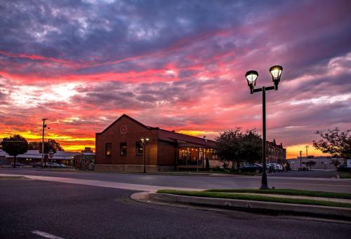 A vibrant sunset casts colorful hues over a brick building and street lamps in a quiet urban setting.
