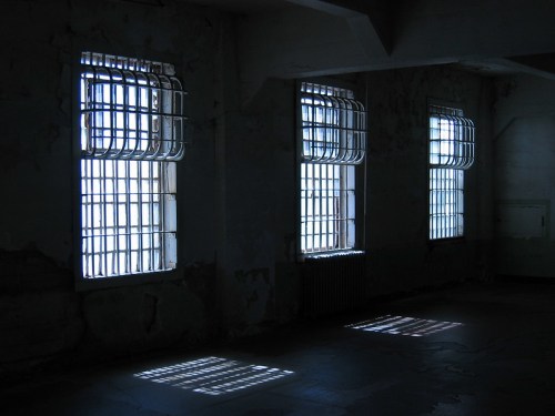 Four barred windows in a dimly lit room, casting shadows on the floor.
