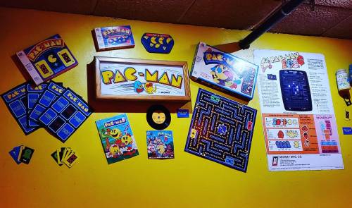 A vibrant wall display featuring various Pac-Man memorabilia, including game boxes, cards, and a game board.
