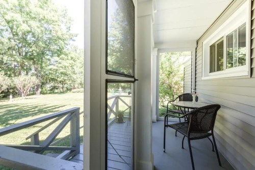 A cozy porch with a table and chairs, overlooking a green yard and trees in bright daylight.