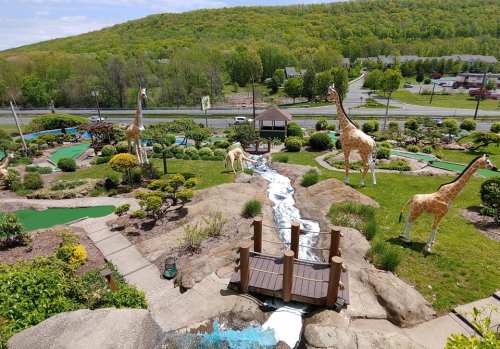 A mini-golf course featuring large giraffe sculptures, a waterfall, and lush greenery under a clear blue sky.