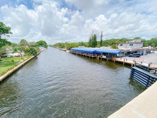 A calm river scene with a blue-roofed building on the bank, surrounded by trees and partly cloudy skies.