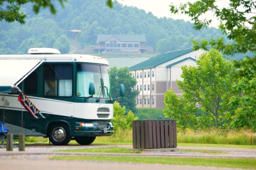 An RV parked near a grassy area, with a building and green hills in the background.