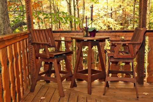 A cozy wooden deck with two high chairs and a small table, surrounded by autumn foliage.