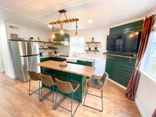 Modern kitchen with green cabinets, a wooden island, pendant lights, and a cozy dining area with four stools.