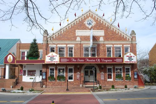 Historic brick building with a marquee reading "The State Theatre of Virginia," adorned with flags and decorative elements.