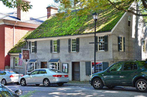 Historic building with a moss-covered roof, surrounded by parked cars and trees. American flag displayed.