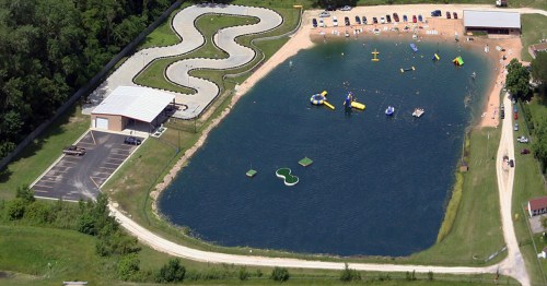 Aerial view of a recreational area featuring a go-kart track, a lake with inflatable water toys, and parking spaces.