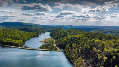 Aerial view of a winding river surrounded by lush green forests and rolling hills under a partly cloudy sky.