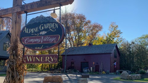 Sign for "Alpine Garden Camping Village and Winery" with a rustic building and autumn foliage in the background.