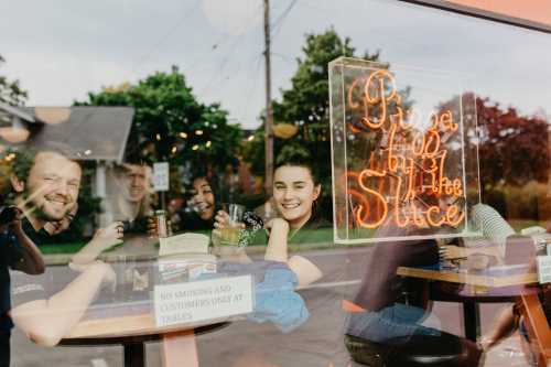 A group of friends smiling and enjoying drinks at a café, with a neon sign in the window.