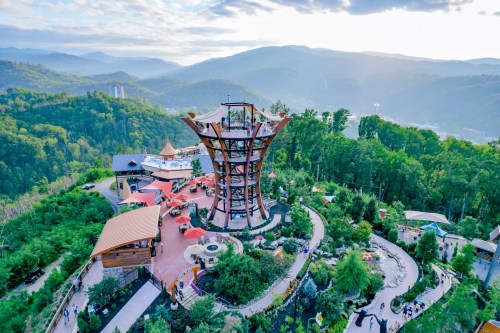 Aerial view of a scenic lookout tower surrounded by lush greenery and mountains under a cloudy sky.