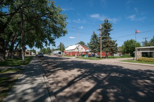 A quiet street scene featuring a red building, trees, and a clear blue sky.