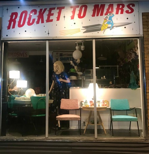 A storefront display with a "Rocket to Mars" sign, featuring colorful chairs and a mannequin in a blue outfit.