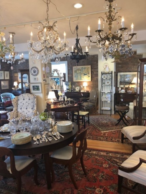 A cozy antique shop filled with elegant furniture, chandeliers, and decorative items, showcasing a warm, inviting atmosphere.