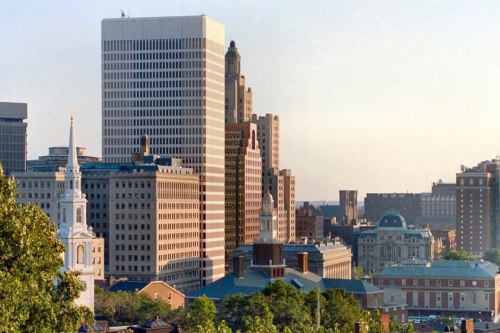 A city skyline featuring modern and historic buildings, with a church steeple in the foreground.