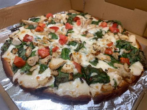 A pizza topped with grilled chicken, spinach, and tomatoes, served in a cardboard box.