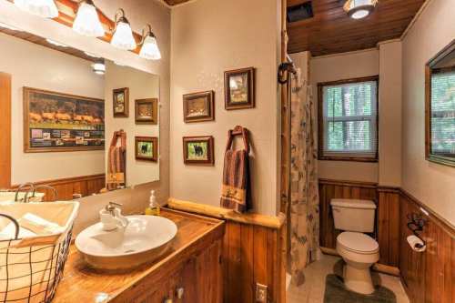 Cozy bathroom with wooden accents, a sink, toilet, and shower, featuring framed pictures and natural light.