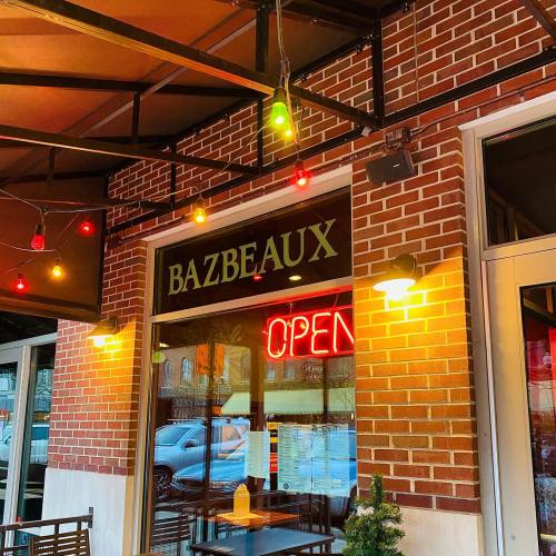 Exterior of Bazbeaux restaurant with a bright "OPEN" sign and colorful string lights.