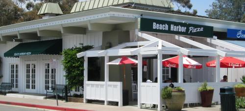 Exterior of Beach Harbor Pizza, featuring outdoor seating with red umbrellas and a white wooden structure.