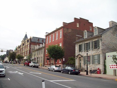 Historic buildings line a street, featuring a mix of architectural styles and parked cars along the curb.