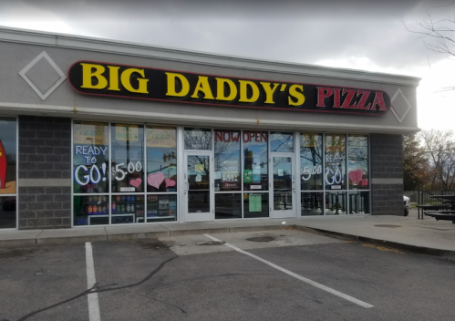 Exterior of Big Daddy's Pizza with a "Now Open" sign and promotional window displays.