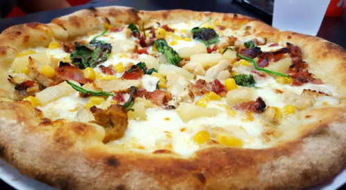 A close-up of a pizza topped with chicken, corn, spinach, and pineapple on a golden crust.