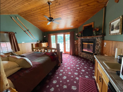 Cozy bedroom with wooden ceiling, fireplace, and sliding doors leading to a patio, decorated with ski gear.