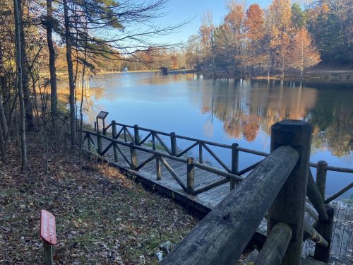 A serene lake surrounded by trees, with a wooden dock and autumn foliage reflecting in the water.
