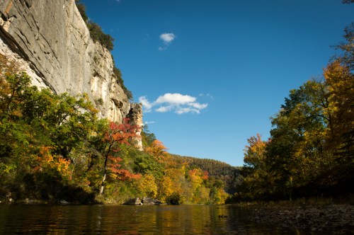 A serene river scene surrounded by colorful autumn foliage and towering cliffs under a clear blue sky.