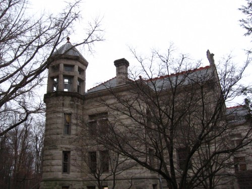 Historic stone building with a turret, surrounded by bare trees against a gray sky.