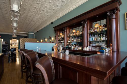 A wooden bar with ornate columns, shelves filled with bottles, and a stylish interior featuring a patterned ceiling.