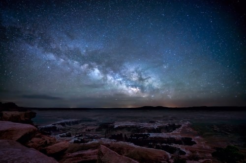 A stunning night sky filled with stars and the Milky Way over a calm ocean shoreline.