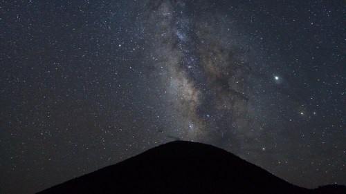 A starry night sky filled with the Milky Way above a dark mountain silhouette.