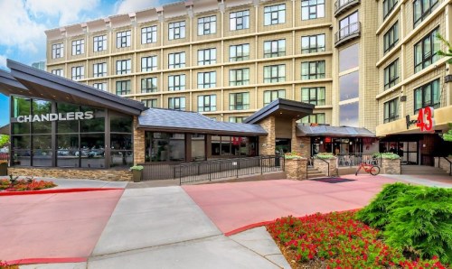 Exterior view of a hotel with a restaurant named "Chandlers" and a modern entrance, surrounded by landscaped gardens.
