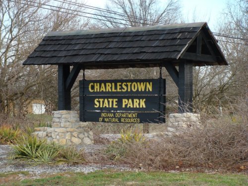 Sign for Charlestown State Park, featuring black wooden structure with stone base and natural surroundings.